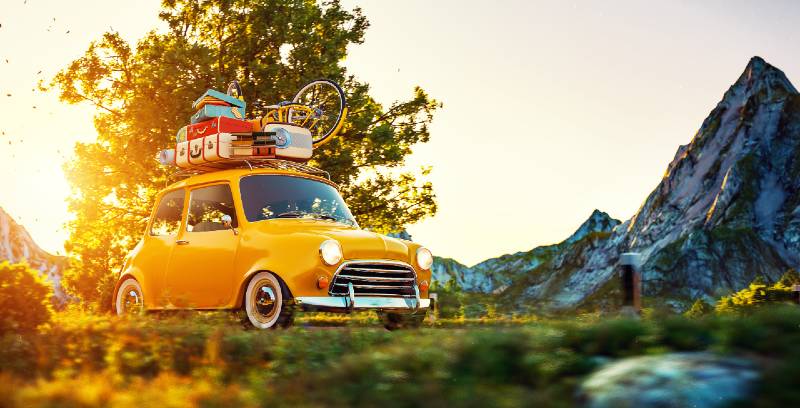 Cute little retro car with suitcases and bike on top drives through wonderful country road car camping