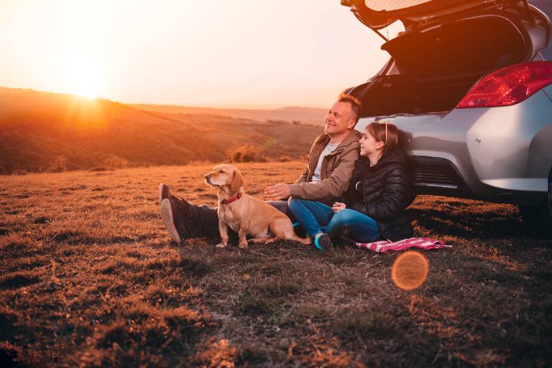 Father and daughter with small yellow dog camping on a hill while sitting on the ground by the car-car camping