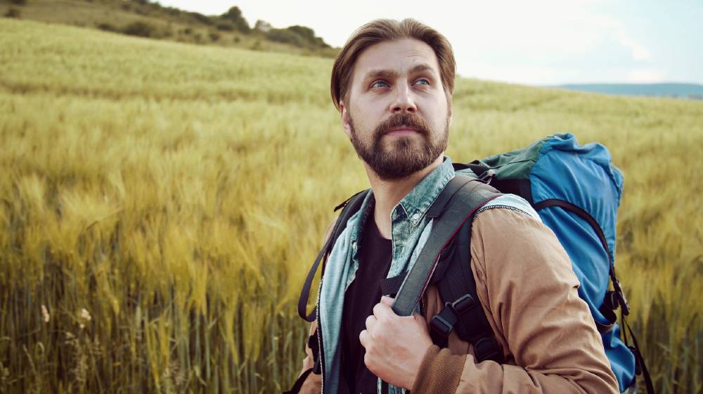Half-turn portrait of bearded backpacker hiking in countryside admiring landscape | How to Pack a Hiking Bug Out Bag or Backpack | featured