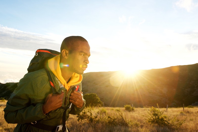 Side portrait of African American man hiking in the mountains with sunset in the background - Bug Out Bag