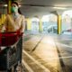 Woman wearing mask groceriessupplies shopping in supermarket,pushing trolley.Food supplies shortage | 8 Uncommon Prepping Supplies | featured
