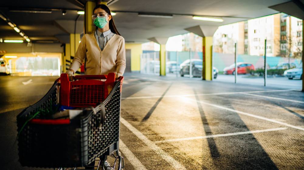 Woman wearing mask groceriessupplies shopping in supermarket,pushing trolley.Food supplies shortage | 8 Uncommon Prepping Supplies | featured