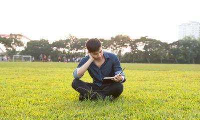 Young male student reads a book on grass field in the afternoon in campus | College Survival Kit - Essential Items You Need in College | featured