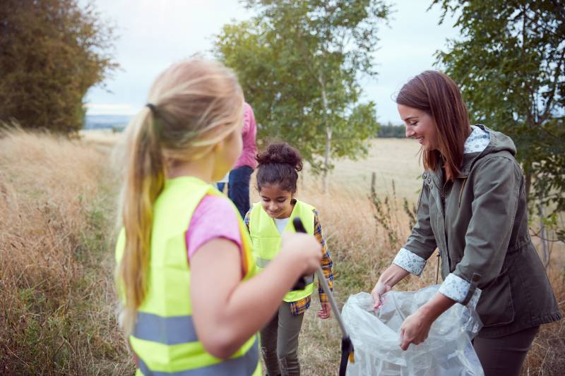 Adult team leader with group of kids in outdoor activity camp collecting trash together |  Safety rules when camping