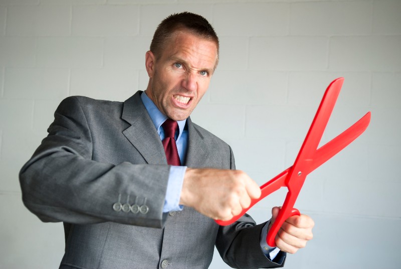 Businessman holding a pair of big red scissors making some serious cuts in copy space-Survival Economic Collapse
