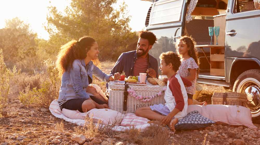Family having a picnic beside their camper van, full length | Camping Holidays - Advantages and Disadvantages | featured