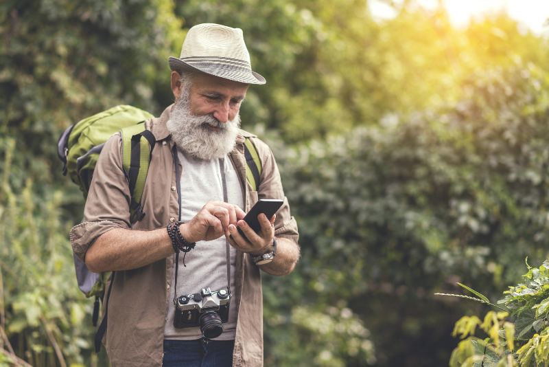 Joyful mature male tourist offering smartphone safety tips to active seniors