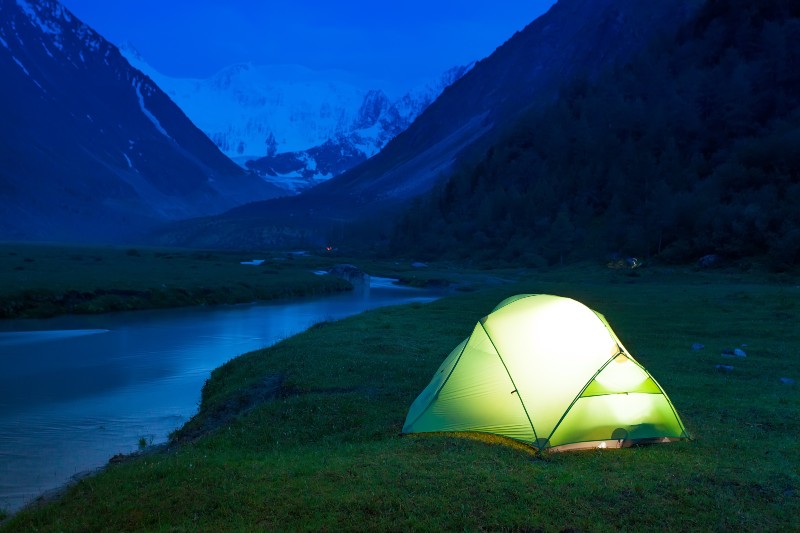 Glowing tent stands on the banks of a mountain stream | safety camping tips