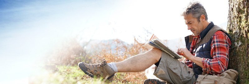 Hiker relaxing by tree looking at map and using tablet-Hiking Safety Tips For Active Seniors