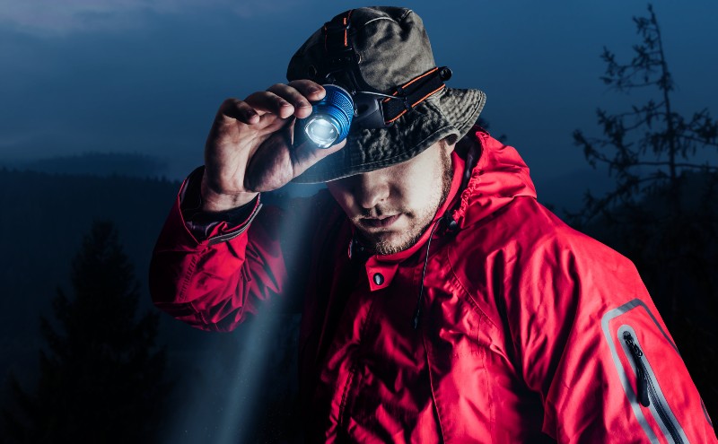Photo of a male hiker in red jacket and panama putting on head mount flashlight-Truck Bed Camping