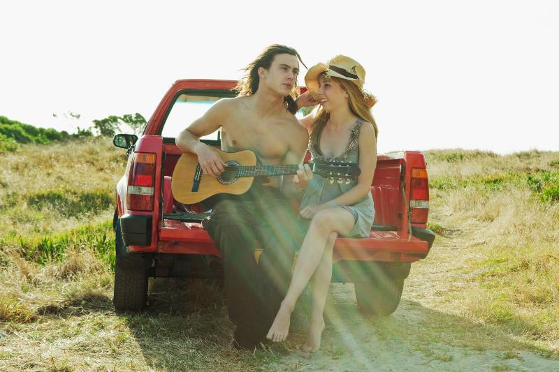 Young man playing guitar to young woman-Truck Bed Camping