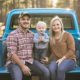 mom, dad and baby toddler son family sitting on a vintage blue pick-up truck bed-Truck Bed Camping