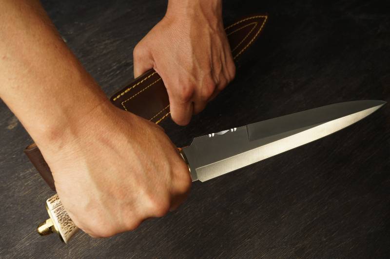 l'homme tient un grand couteau à double tranchant avec un manche en os - doit chercher dans un couteau de survie