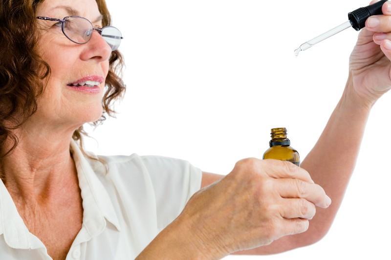 Close-up of mature woman holding dropper with medicine against white background-Colloidal Silver