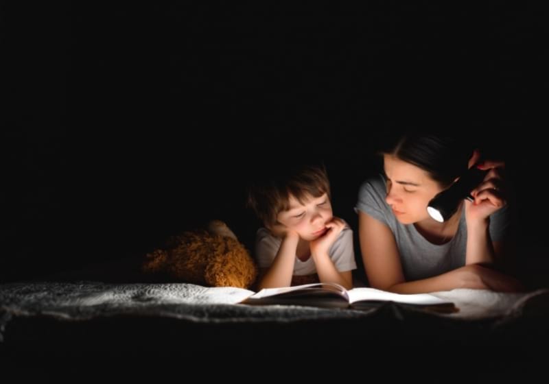 happy family mother and child son reading a book with a flashlight | National Grid Outage | How to Prepare for Power Grid Failure
