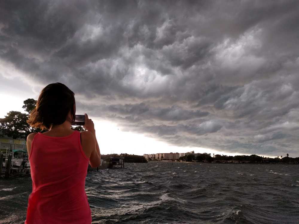 A young woman photographs dark clouds as a storm approaches | How to Prepare for Climate Change | 10 Ways For Climate Change Preparedness | featured