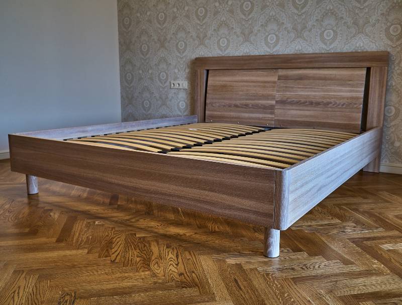 Bed made of solid oak. Bed on the background of patterned wallpaper-bed frame joinery