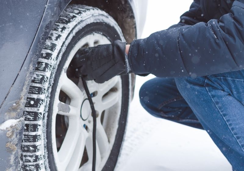Driver is inflating a tire by car air compressor on the winter road | Winterize Car | 13 Ways on How to Winterize a Car