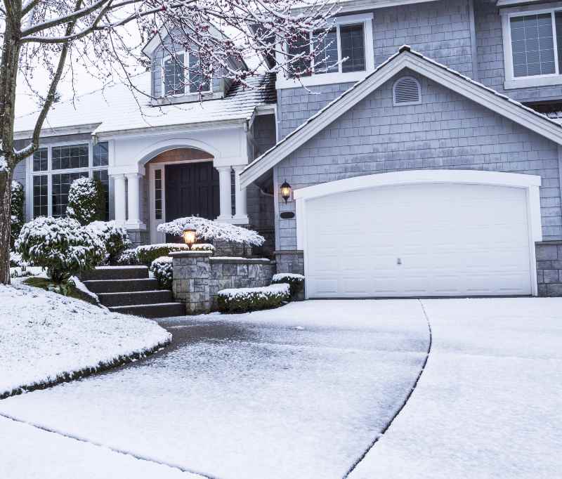 photo of suburban home with snow on drive way, lawn, plants, trees and roof | How to Melt Snow on Driveway