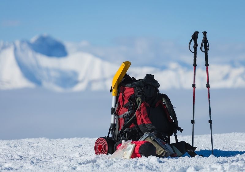 Backpack and hiking poles of a hiker in the snow | Avalanche Gear Checklist for Your Avalanche Survival Kit