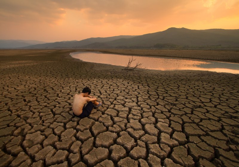 Sad Children or young man sitting on cracked earth near drying river metaphor water crisis, climate change, Drought and Environment disaster _ How Will Society Collapse 2040