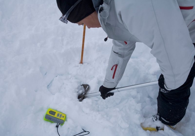 Young woman searching for avalanche victims in snow | beacon shovel probe kit