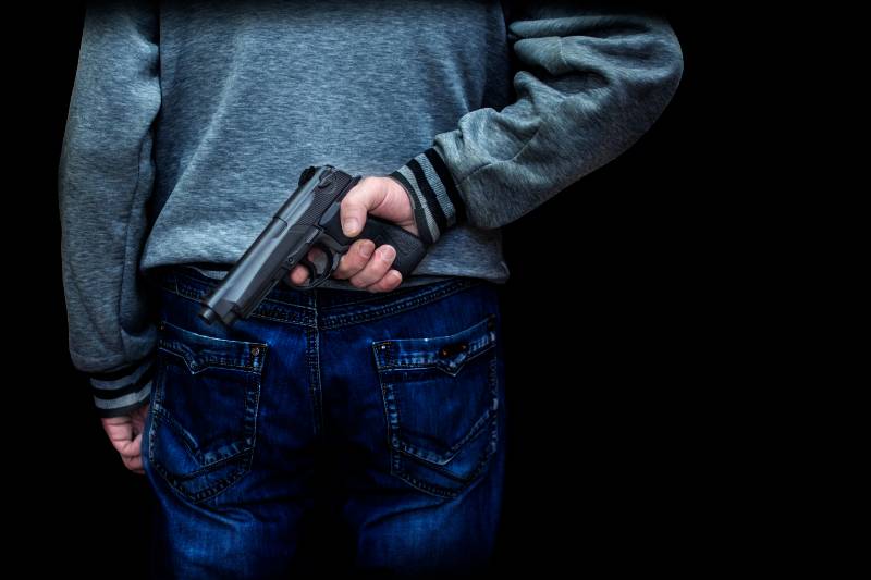 man holding a gun behind his back against a black background | Mass Shooting