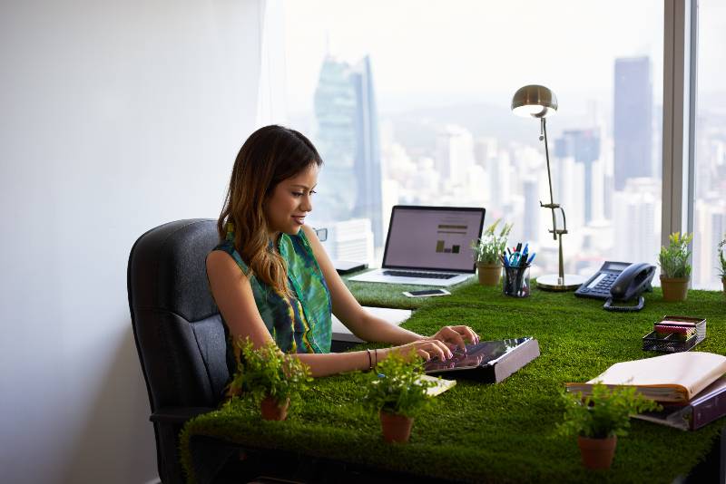 Concept of ecology and environment Young business woman working in modern office with table covered of grass and plants Environmental Policy ss 1
